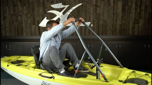 A person demonstrating the Hobie H-Bar's utility to assist the user from a seated to a standing position on a Hobie Passport 12 kayak