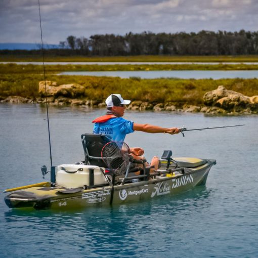 Image shows the Livewell XL installed on a Hobie Pro Angler 14 as the kayaker casts his line. 2 vertical rod holders are mounted to the tank with 1 rod being housed