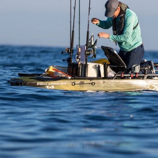 Image shows the Livewell XL installed on a Hobie Pro Angler 14 as the kayaker leans over his seat to add his catch to the tank. Multiple vertical rod holders are mounted to the tank with 4 rods housed