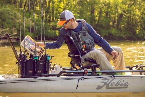 An angler aboard a Hobie fishing kayak retrieves a tackle box from a YakAttack BlackPak Pro Kayak Fishing Crate - 16" x 16"