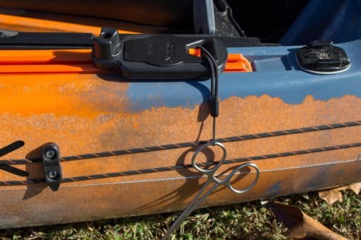 A YakAttack Retractable Gear Tether shown mounted to a fishing kayak with a pair of scissors tethered to the unit